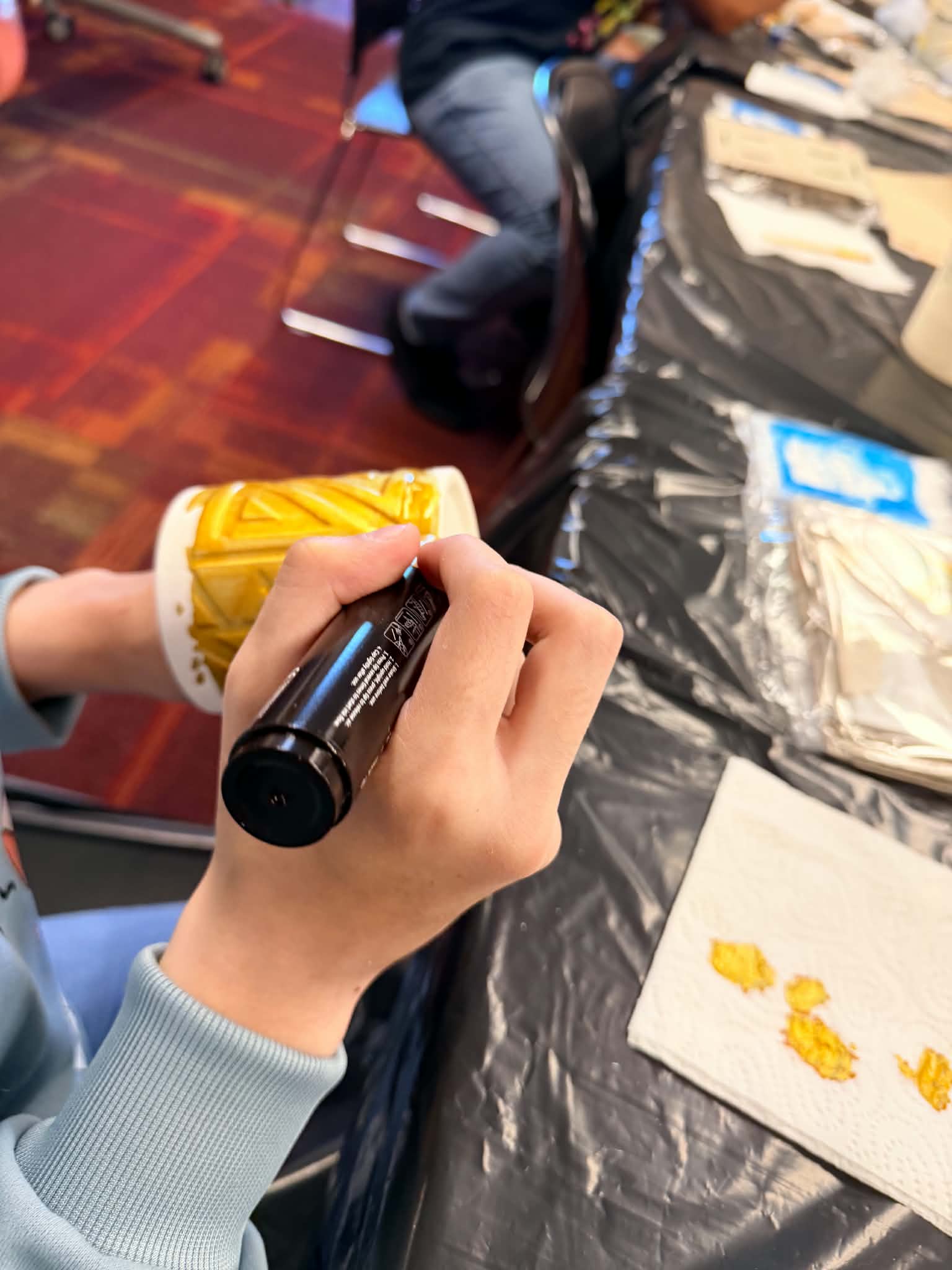 A close-up of paint supplies and a participant’s hand during a Rising Up Now art workshop.