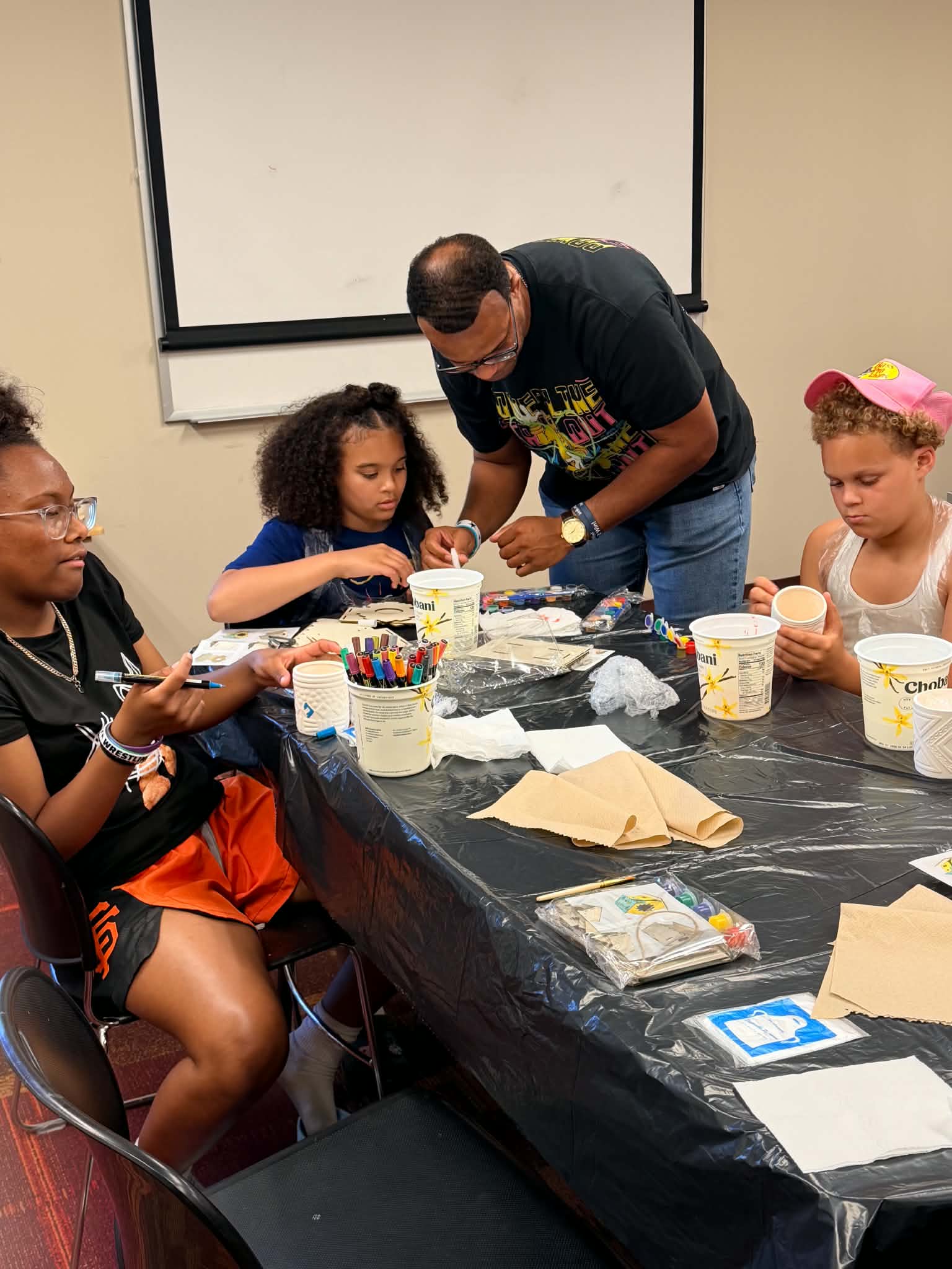 An adult helper assisting children during a seated art workshop activity.